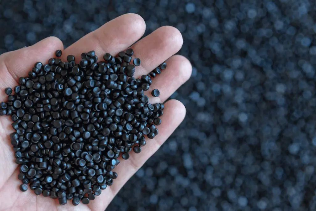 Grondstof voor EPS: een hand houdt donkergrijze polystyreenkorrels vast.